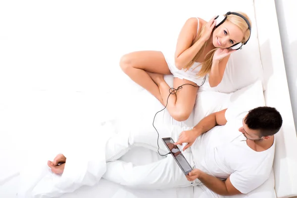 Молодая пара в постели, используя планшетный компьютер, чтобы слушать музыку — стоковое фото