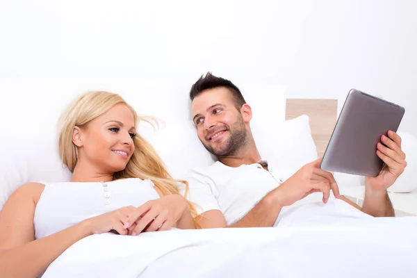 Schönes junges Paar mit einem Tablet-PC im Bett — Stockfoto