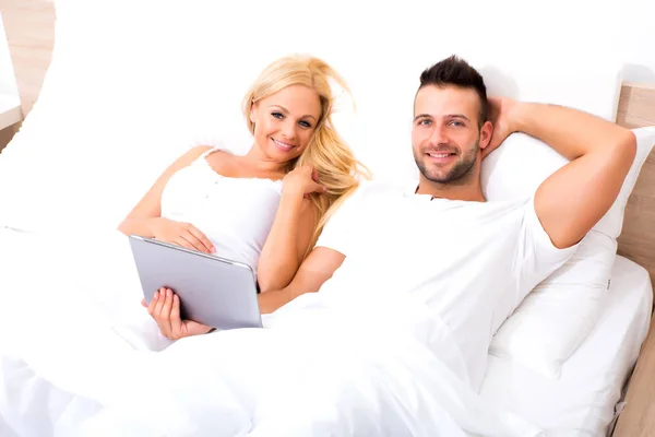 Beau jeune couple utilisant une tablette PC au lit — Photo