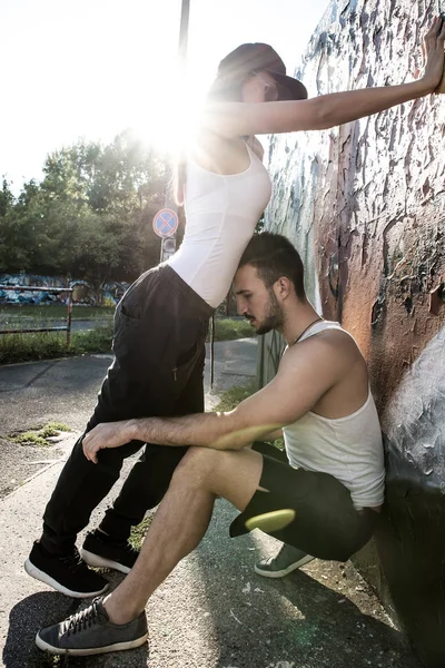 Casal jovem em pé em uma parede em um ambiente urbano — Fotografia de Stock