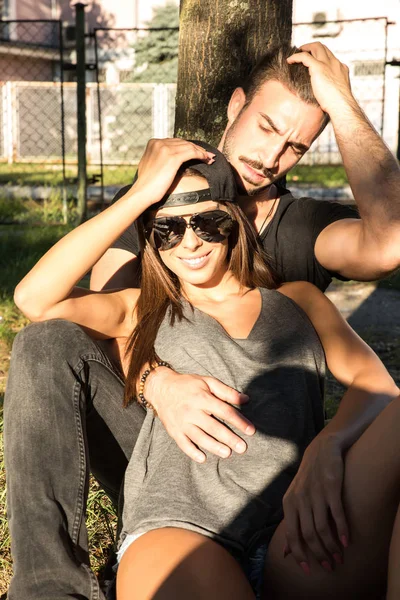 Pareja joven sentada contra un árbol en un entorno urbano — Foto de Stock