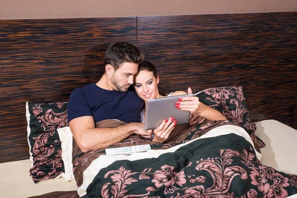 Smukke unge par ved hjælp af en Tablet PC i sengen - Stock-foto