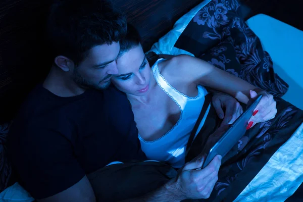 Smukke unge par ved hjælp af en Tablet PC i sengen - Stock-foto
