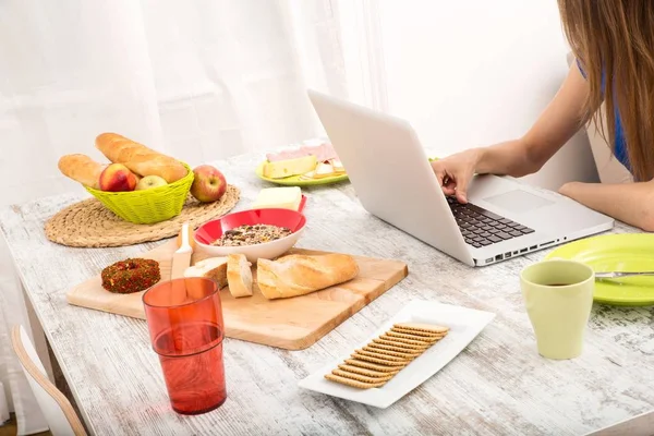 Junge Frau frühstückt während sie einen Laptop benutzt — Stockfoto