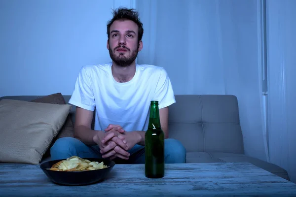 Молодой человек, смотреть фильм печальный ночью с чипсы и пиво — стоковое фото