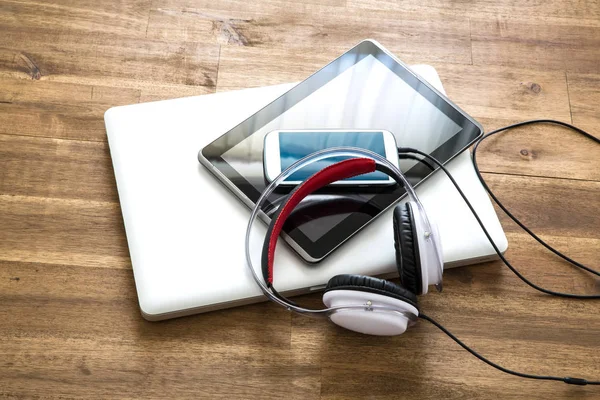 Digitale Geräte und Kopfhörer auf einem hölzernen Schreibtisch — Stockfoto