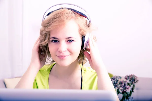 Ung vuxen kvinna med hörlurar framför en laptop — Stockfoto