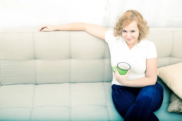 Jovem com uma xícara de café no sofá — Fotografia de Stock