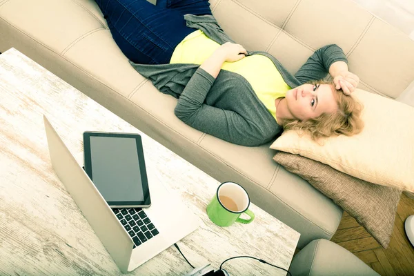 Giovane donna sul divano con gadget — Foto Stock