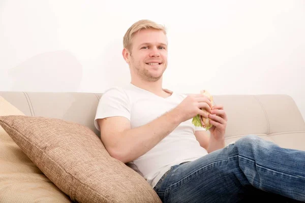 Jeune homme mangeant un sandwich à la maison — Photo