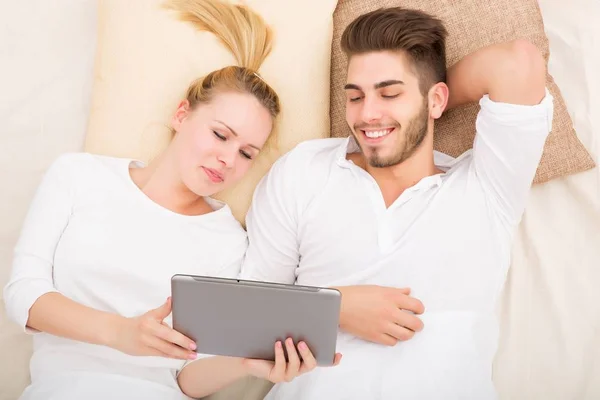 Jeune couple avec une tablette PC au lit — Photo