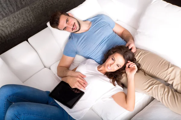 Casal jovem usando um Tablet PC juntos no sofá em casa — Fotografia de Stock