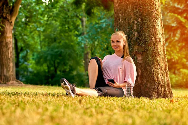 Junge Frau sitzt an einem Baum in einem Park — Stockfoto