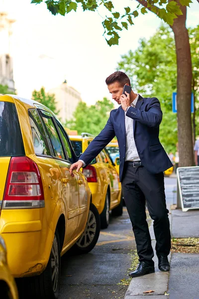 Молодой бизнесмен идет к такси и разговаривает по телефону — стоковое фото