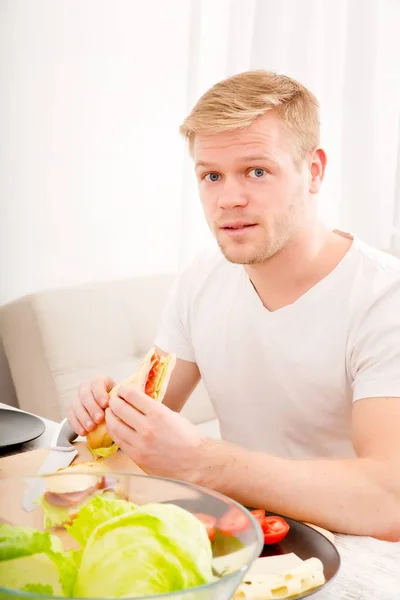 Ung man äter en smörgås hemma — Stockfoto