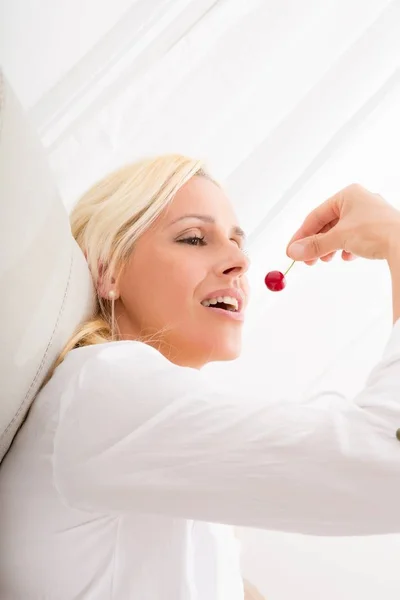 Mulher comendo cereja no sofá — Fotografia de Stock