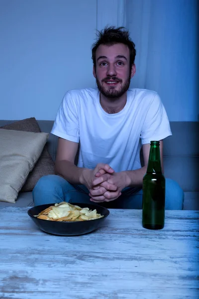 Jovem assistindo TV à noite com batatas fritas e cerveja — Fotografia de Stock