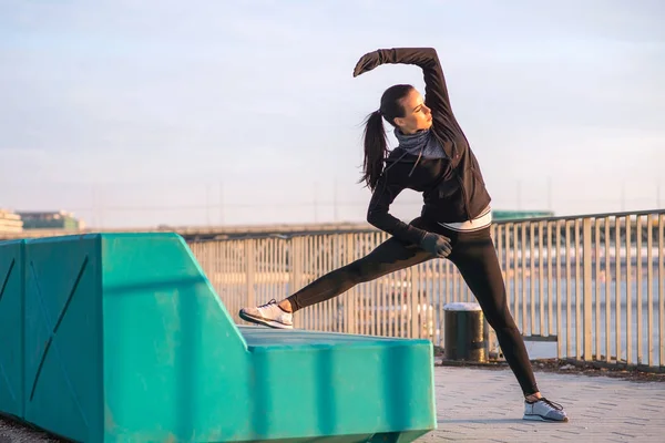 Una mujer joven deportiva que se extiende en la puesta del sol — Foto de Stock