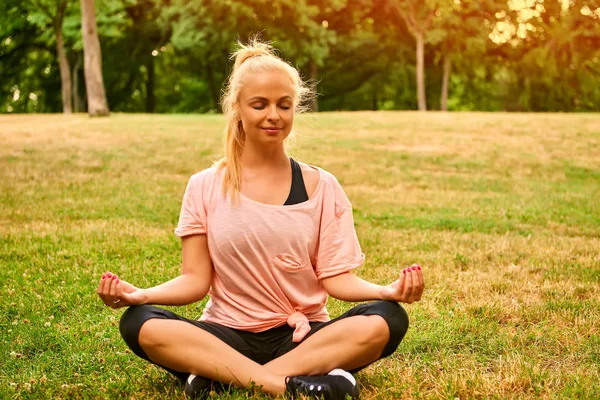 Jonge vrouw mediteren op een veld in een park — Stockfoto