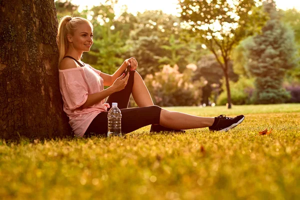 Young woman sitting at a tree in a park — Stock Photo, Image