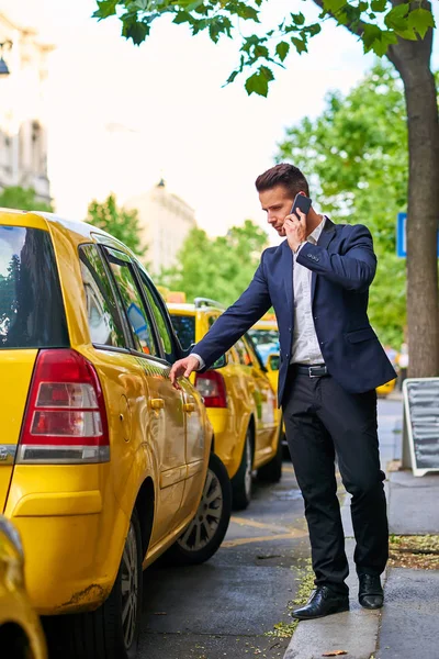 Молодой бизнесмен идет к такси и разговаривает по телефону — стоковое фото
