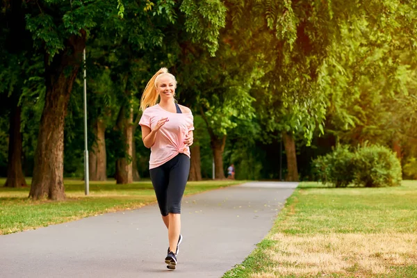 Young woman running on the road in a park — Stock Photo, Image