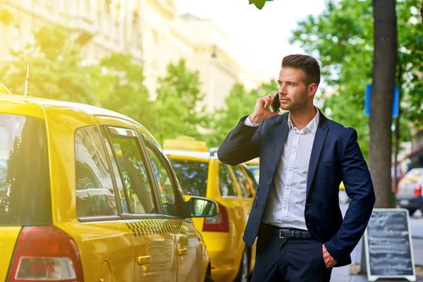Молодой бизнесмен разговаривает по телефону и ждет такси — стоковое фото