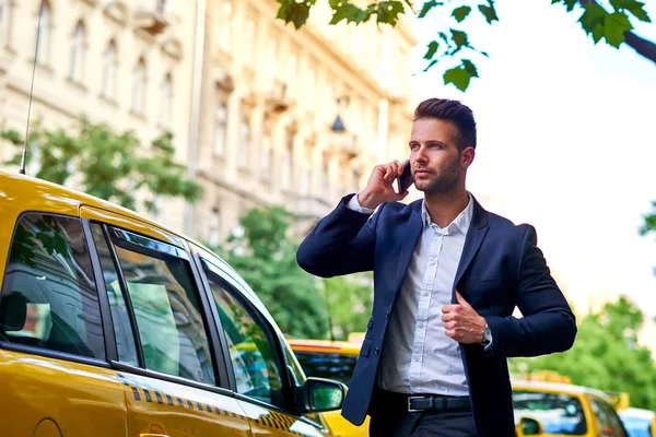 Молодой бизнесмен разговаривает по телефону и ждет такси — стоковое фото