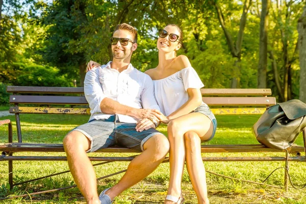 Красивая молодая пара отдыхает в солнечный летний день на скамейке — стоковое фото