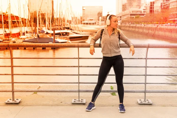 橋の手すりの横で音楽を聴いている運動選手の女性 — ストック写真