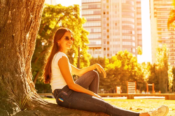 Mladá žena sedící vedle stromu a užívající si sluníčka — Stock fotografie