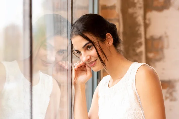 Portrait of a beautiful young woman standing at a window — Stock Photo, Image