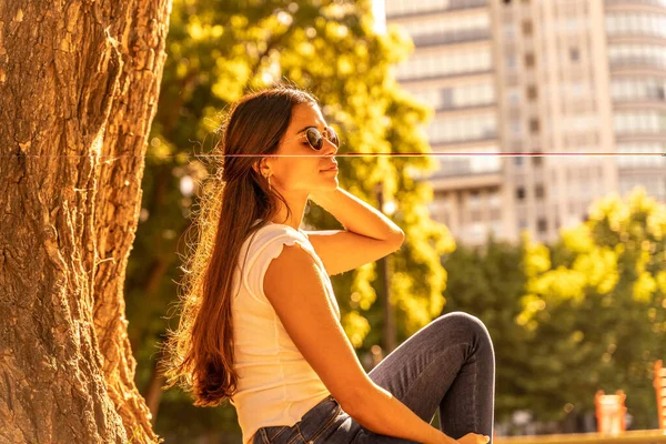 Молода жінка сидить поруч з деревом і насолоджується сонцем — стокове фото