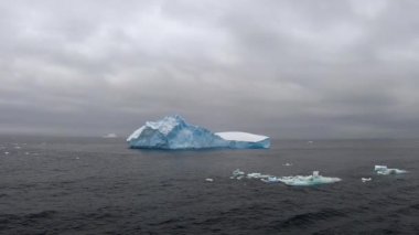 Antarktika 'daki Amiralty Körfezi' nde daha küçük dağları olan bir buzdağı. Hareket halindeki bir gemiye kilitlenen kamera, sağdan sola hareket ettiriyor..