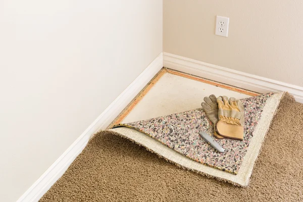 Gloves and Utility Knife On Pulled Back Carpet and Pad In Room. — Stock Photo, Image