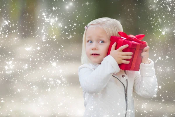 Dziewczynka trzymając czerwony świąteczny prezent na zewnątrz z mocą śnieg — Zdjęcie stockowe
