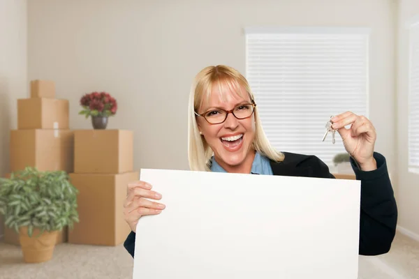 Mulher com sinal em branco e chave da casa no quarto vazio com Mo embalado — Fotografia de Stock