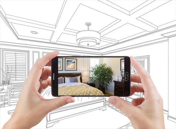 Руки тримають смартфон відображає фотографію спальні малюючи позаду — стокове фото