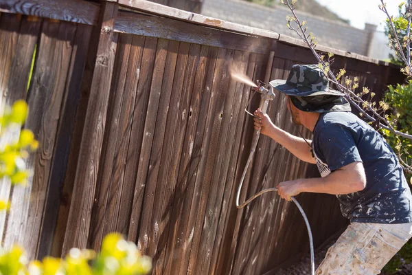Pintor profesional rociando valla de patio con mancha —  Fotos de Stock