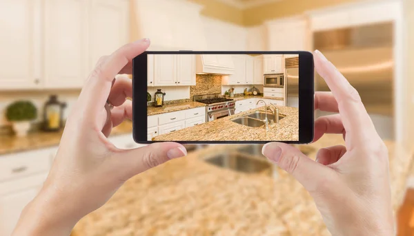 Руки женщины держат смартфон с фотографией кухни за спиной . — стоковое фото