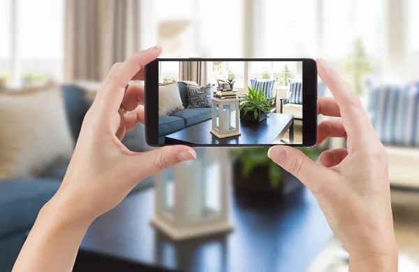 Female Hands Holding Smart Phone Displaying Photo of House Interior Living Room Behind. — Stock Photo, Image