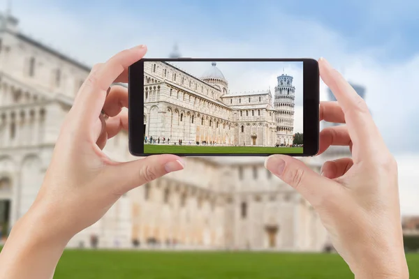 Mãos femininas segurando telefone inteligente exibindo foto da torre inclinada de Pisa atrás — Fotografia de Stock