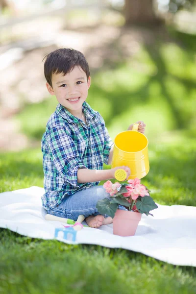 Gemengd ras jongen drenken zijn ingemaakte bloemen buiten op de — Stockfoto