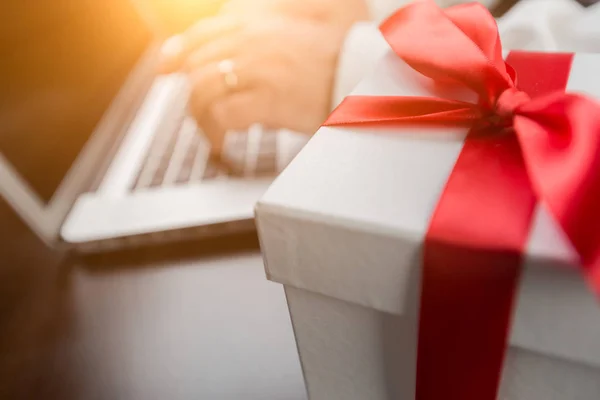 Weißer Geschenkkarton mit roter Schleife und Schleife in der Nähe von Mann tippt auf Laptop — Stockfoto