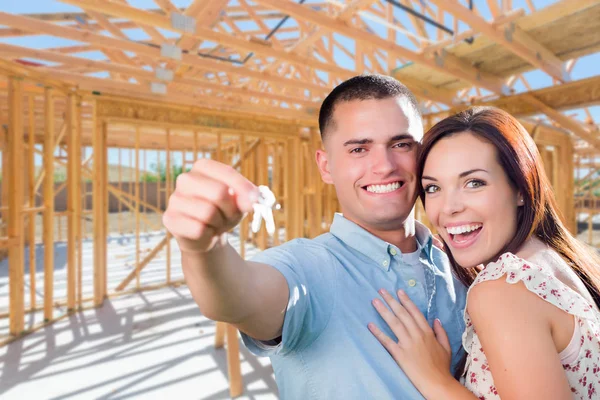 Young Military Couple On Site With House Keys Inside Their New Home Construction Framing. — Stock Photo, Image