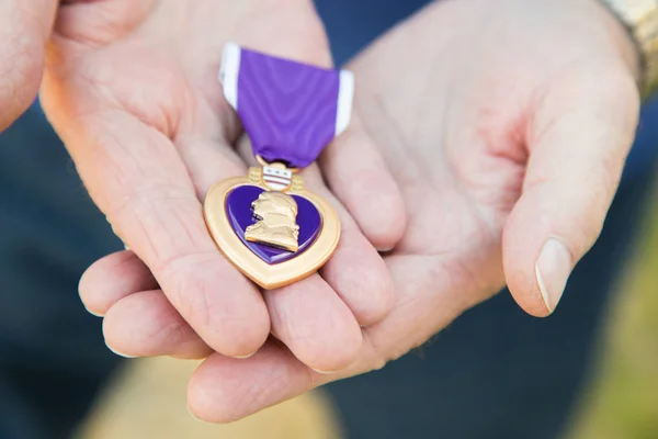 Homem sênior segurando a medalha militar do coração roxo em suas mãos . — Fotografia de Stock