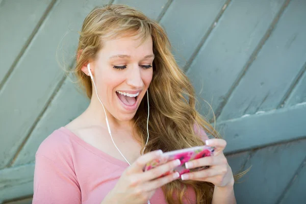 Porträt einer jungen erwachsenen Frau mit braunen Augen, die mit Kopfhörern auf ihrem Smartphone Musik hört. — Stockfoto