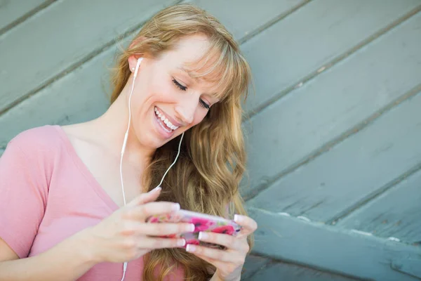 Outdoor Portret van jonge volwassen Brown Eyed vrouw luisteren naar muziek met koptelefoon op haar Smart Phone. — Stockfoto