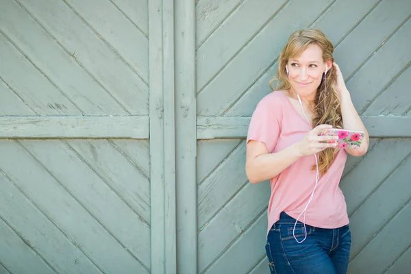 Portrait extérieur d'une jeune femme aux yeux bruns adulte écoutant de la musique avec des écouteurs sur son téléphone intelligent . — Photo