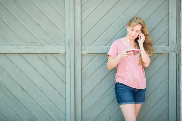 Utomhus porträtt av unga vuxna Brown Eyed Woman lyssnar på musik med hörlurar på sin smarta telefon. — Stockfoto